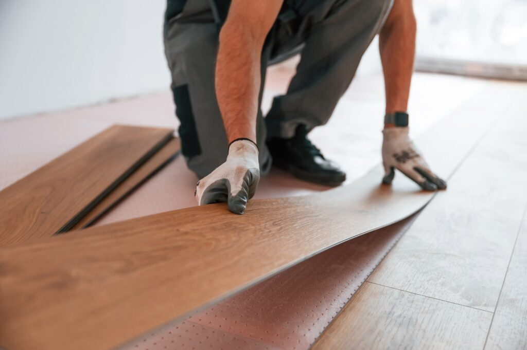 Worker installing light brown hardwood flooring over pink underlayment with precision