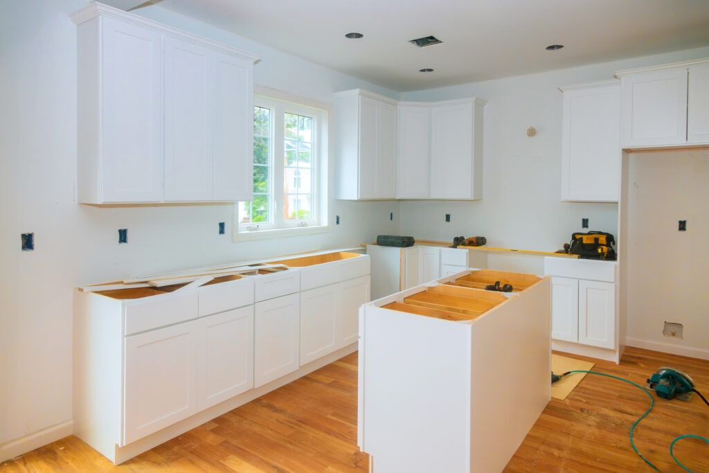 Kitchen renovation in progress with cabinet installation and wood flooring on a sunny day