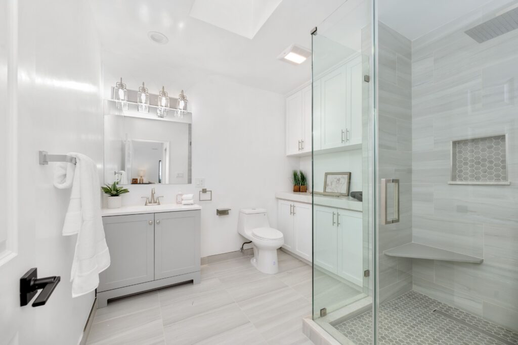Modern white bathroom with glass shower, sleek cabinetry, and stylish lighting fixtures.