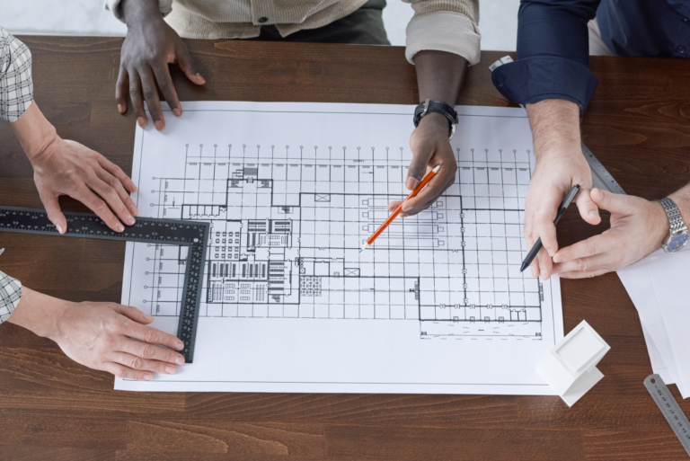 High angle view of engineers drawing with pencil and measuring with ruler they working over blueprint at the table
